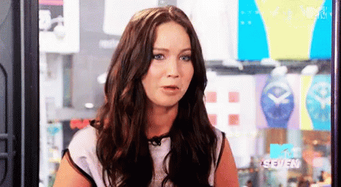 A Woman With Long Brown Hair And Blue Eyes Is Sitting In Front Of A Mtv Seven Sign . GIF
