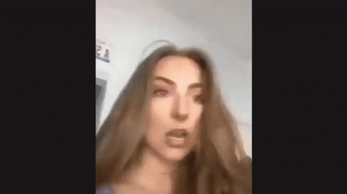 A Woman With Long Brown Hair Is Making A Funny Face And Looking At The Camera . GIF