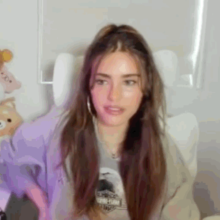 A Woman With Long Brown Hair Is Sitting In A Chair And Making A Face . GIF