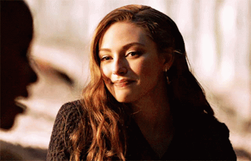 A Woman With Long Brown Hair Is Smiling And Looking At A Man . GIF