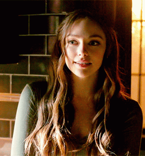 A Woman With Long Brown Hair Is Smiling In Front Of A Tiled Wall GIF