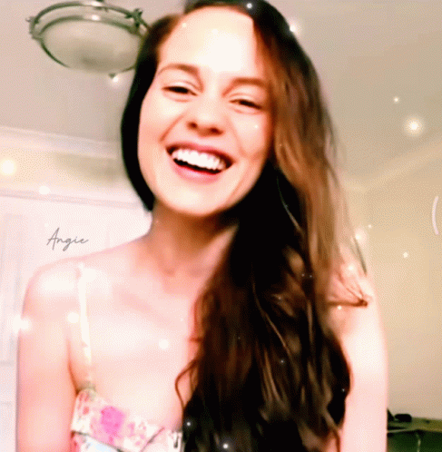 A Woman With Long Brown Hair Is Smiling With Angie Written On Her Chest GIF