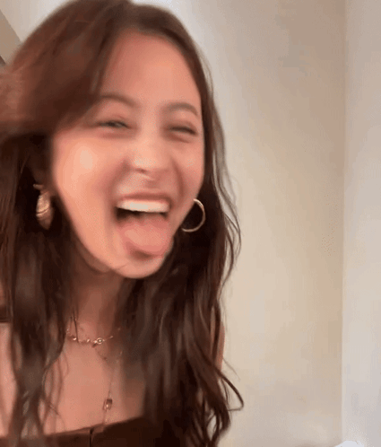 A Woman With Long Brown Hair Is Sticking Her Tongue Out And Laughing . GIF