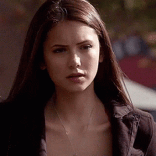 A Woman With Long Brown Hair Is Wearing A Necklace And A Jacket . GIF