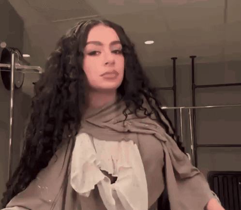 A Woman With Long Curly Hair And A Scarf Around Her Neck GIF