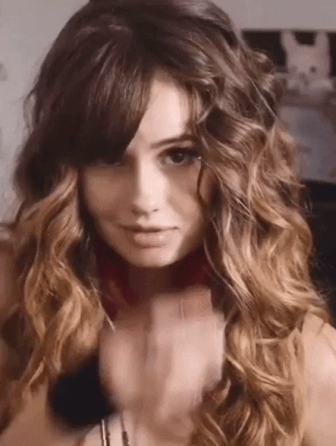 A Woman With Long Curly Hair And Bangs Is Wearing A Choker Necklace . GIF