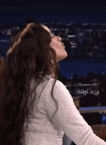 a woman with long curly hair is blowing a kiss at night