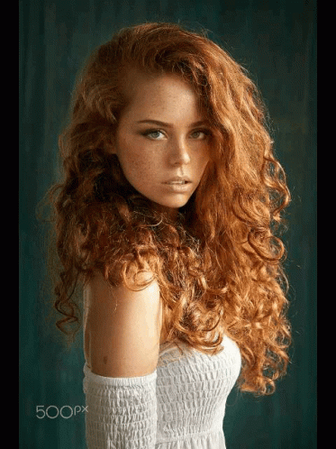 A Woman With Long Curly Red Hair And Freckles Is Wearing A White Dress GIF