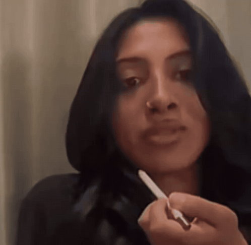 A Woman With Long Dark Hair Is Holding A Pen In Her Hand GIF