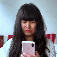 A Woman With Long Dark Hair Is Holding A Pink Iphone In Her Hand . GIF