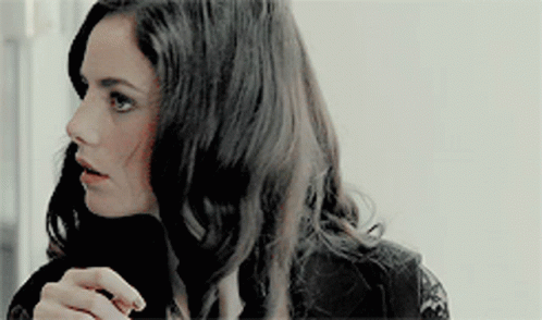 A Woman With Long Dark Hair Is Wearing A Black Lace Top And A Black Turtleneck . GIF