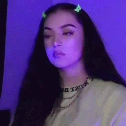 A Woman With Long Dark Hair Is Wearing A Necklace And A Hair Clip . GIF