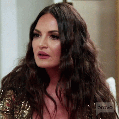A Woman With Long Dark Hair Is Wearing A Sequined Top With Bravo Written On The Bottom GIF