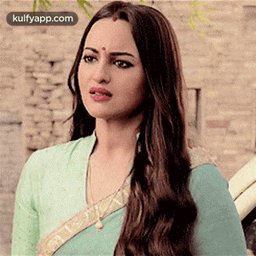 A Woman With Long Hair And A Bindi On Her Forehead Is Wearing A Blue Blouse And A Green Saree . GIF