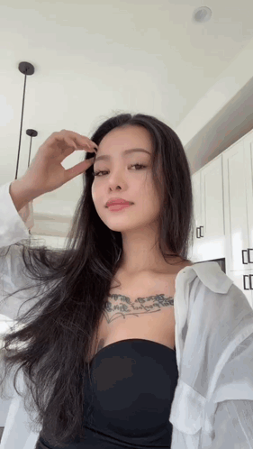 A Woman With Long Hair And A Tattoo On Her Chest Looks At The Camera GIF