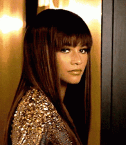 A Woman With Long Hair And Bangs Is Wearing A Gold Sequined Dress . GIF
