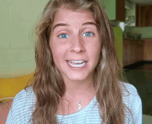 A Woman With Long Hair And Blue Eyes Is Smiling And Wearing A Necklace GIF