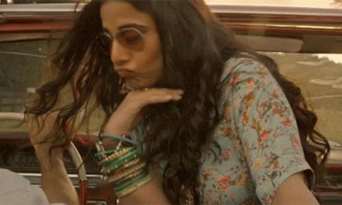 A Woman With Long Hair And Sunglasses Is Sitting In A Car . GIF