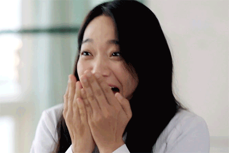 A Woman With Long Hair Is Covering Her Mouth With Her Hands . GIF