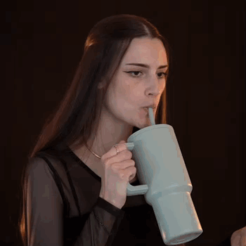 A Woman With Long Hair Is Drinking From A Mug With A Straw . GIF