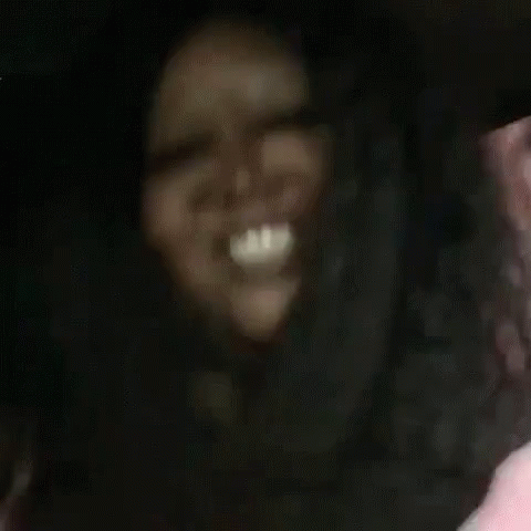 A Woman With Long Hair Is Laughing And Waving At The Camera While Sitting In A Car . GIF
