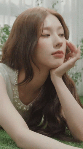 A Woman With Long Hair Is Laying On The Grass With Her Hand On Her Face GIF