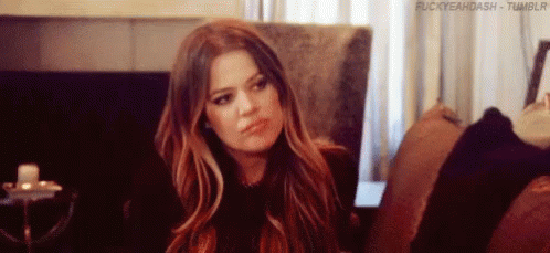 A Woman With Long Hair Is Sitting On A Couch And Making A Funny Face . GIF