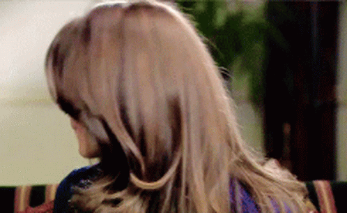 A Woman With Long Hair Is Sitting On A Couch Looking Over Her Shoulder GIF