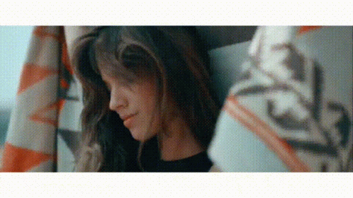 A Woman With Long Hair Is Sitting Under A Blanket And Smiling . GIF