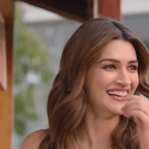 A Woman With Long Hair Is Smiling And Covering Her Mouth GIF