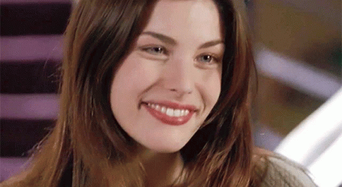 A Woman With Long Hair Is Smiling And Looking At The Camera GIF