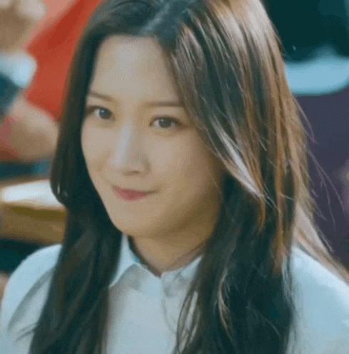A Woman With Long Hair Is Smiling And Wearing A White Shirt GIF