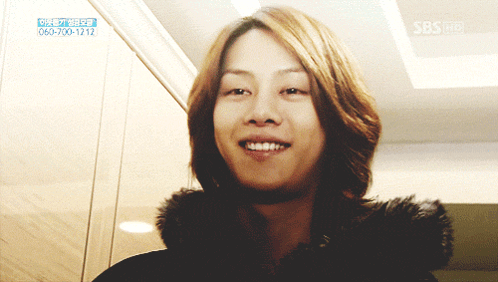 A Woman With Long Hair Is Smiling In Front Of A Sign That Says Sbs On It GIF