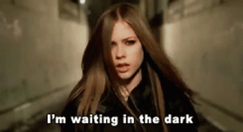 A Woman With Long Hair Is Standing In A Dark Alleyway And Saying I 'M Waiting In The Dark . GIF