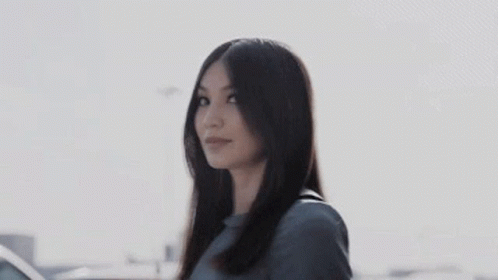 A Woman With Long Hair Is Standing In Front Of A Car And Smiling . GIF