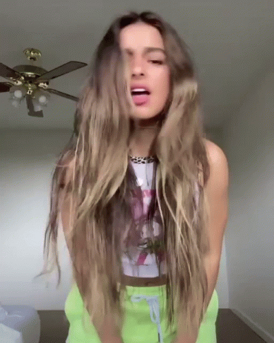A Woman With Long Hair Is Standing In Front Of A Ceiling Fan And Sticking Out Her Tongue . GIF