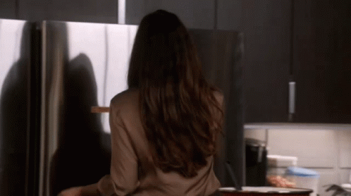 A Woman With Long Hair Is Standing In Front Of A Stainless Steel Refrigerator GIF