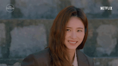 A Woman With Long Hair Is Standing In Front Of A Stone Wall . GIF
