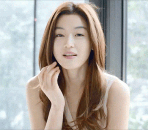 A Woman With Long Hair Is Standing In Front Of A Window GIF