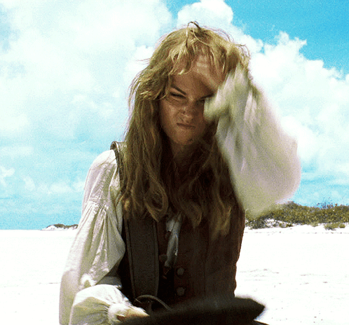 A Woman With Long Hair Is Standing On A Beach With Her Hand On Her Head GIF