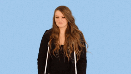 A Woman With Long Hair Is Standing With Crutches And Making A Funny Face . GIF