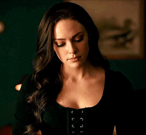 A Woman With Long Hair Is Wearing A Black Lace Up Top And Looking At The Camera . GIF
