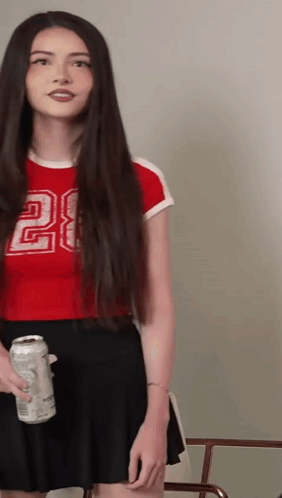 A Woman With Long Hair Is Wearing A Red Crop Top With The Number 28 On It GIF