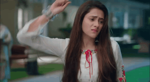 A Woman With Long Hair Is Wearing A White Shirt And Bracelets And Is Making A Funny Face . GIF