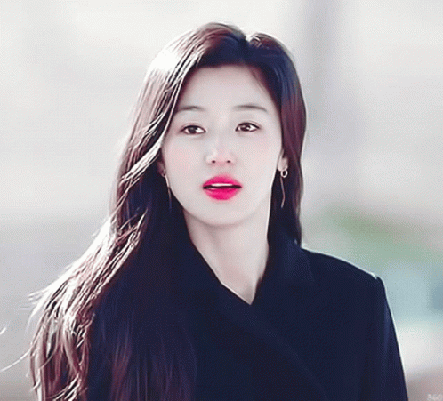 A Woman With Long Hair Is Wearing Earrings And A Black Coat GIF
