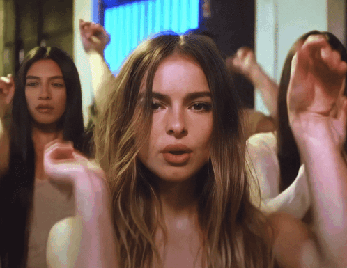 A Woman With Long Hair Stands In Front Of A Group Of Women With Their Hands In The Air GIF