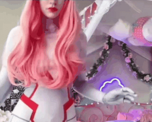 A Woman With Long Pink Hair Is Wearing A Costume And Standing In Front Of A Mirror . GIF