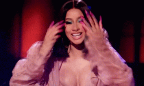 A Woman With Long Pink Nails And A Plunging Neckline Is Smiling While Holding Her Hair . GIF
