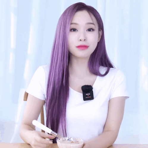 A Woman With Long Purple Hair Is Wearing A White Shirt With A Microphone On Her Neck GIF