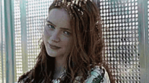 A Woman With Long Red Hair And A Crown On Her Head Is Standing In Front Of A Wall . GIF